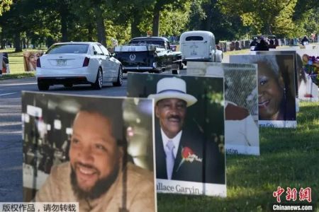 　当地时间8月31日，在美国底特律的贝尔岛公园，一队车辆驶过新冠逝者的照片。