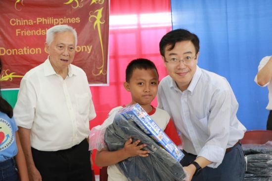中國駐菲大使館參贊謝永輝昨日送禮物給一名兒童。左邊是兒童活動中心創辦人吳啟典。