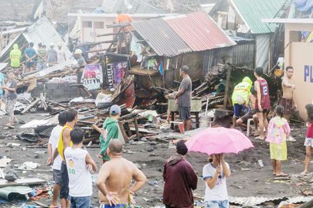 圖為亞眉省黎牙實備市的市民站在被颱風智索伊摧毀的住家前面。