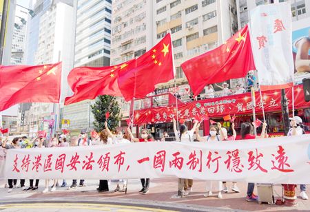 6月30日下午。一眾香港市民來到銅鑼灣街頭舉行「支持港區國安法唱國歌」活動。大家揮舞五星紅旗和香港區旗，高唱國歌與《我和我的祖國》等愛國歌曲，贏得街頭市民的陣陣掌聲。圖為支持國安法的市民與「港島各界慶香港回歸、賀國安立法」巡遊巴士在銅鑼灣街頭相遇。（中新社）