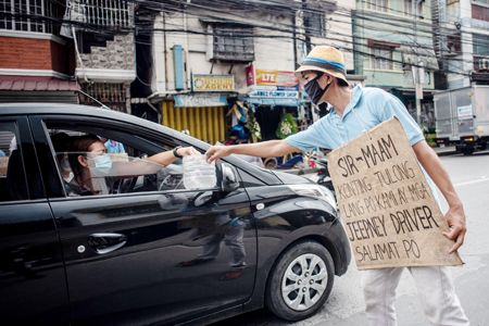 一名集尼尼司機戴著口罩和寫著「先生/女士，請幫助，我們是集尼司機」的牌子在路上接受施捨。8月6日的數據顯示，菲律賓經濟在經歷了40年來最大的季度收縮後，已陷入衰退。由於新冠肺炎疫情的封鎖，菲律賓經濟受到重創，企業受到重創，數百萬人失業。（法新社）