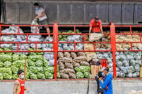 圖為戴著口罩的男子前日在馬尼拉街頭搬運蔬菜。新冠肺炎疫情嚴重，政府宣布大岷區置於一般社區隔離狀態。（新華社）