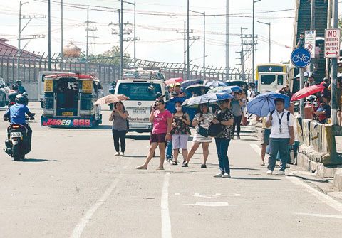 3月3日,在計順市的聯邦大道,通勤者們在等候交通工具時撐起了傘。衛生部也建議民眾在炎熱天氣下,從上午10點至下午4點期間多喝水並減少戶外活動時間。