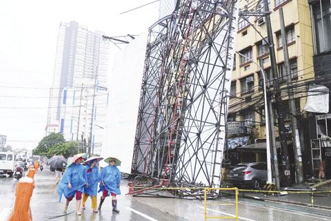 7月19日，計順市，由於熱帶風暴「克里星」離開菲律濱北部地區帶來的增強風雨，穿著雨具的婦女走在倒塌的廣告牌旁。（美聯社）