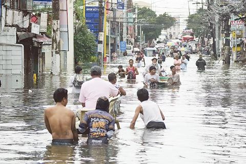 7月25日，馬拉汶市居民在颱風「艾蒙」加劇季風降雨的情況下，涉水通過淹水的道路。（美聯社）
