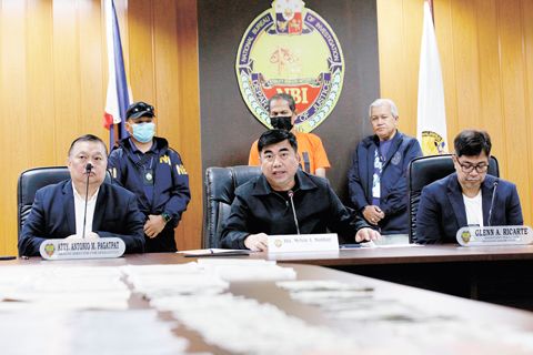 國調局局長梅爾文·馬蒂巴格（居中就坐）於週五在巴西市國調局總部舉行的記者會上，向媒體介紹一名被捕的菲裔美國人，該人士涉嫌持有價值120億披索的偽造美元。這名嫌疑人在巴西市被捕，將面臨分銷和持有偽造美元鈔票、國庫券和聯邦債券的指控。