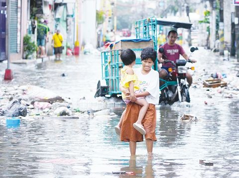 11月10日,那莫沓斯市一名婦女與兒童因超級颱風烏灣及漲潮穿越淹水街道。(美聯社)