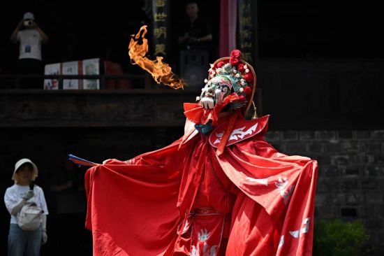 6月14日,游客在万灵古镇观看变脸吐火表演。中新社记者